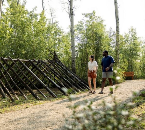Ein Paar geht auf einem Waldweg entlang einer Holzstruktur in einem bewaldeten Bereich. Kanada-Rundreise