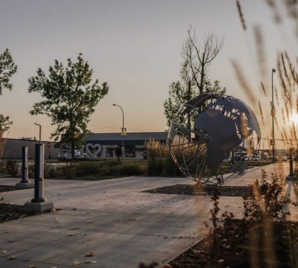 Skulptur einer Weltkugel auf einem Gehweg in Fort St. John, umgeben von Pflanzen. Kanada-Rundreise