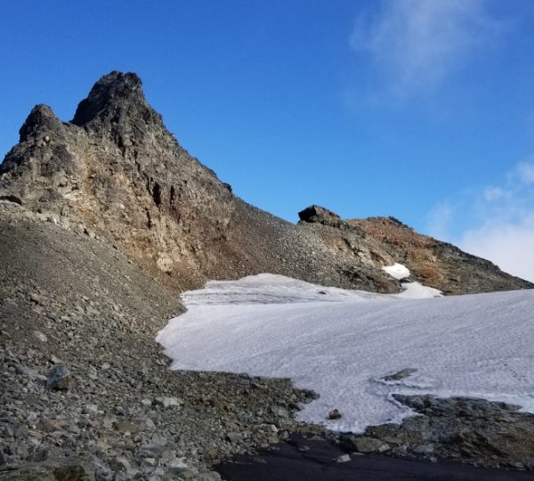Ein steiler Berggipfel mit schneebedecktem Hang und felsigem Gelände unter blauem Himmel. Kanada-Rundreise