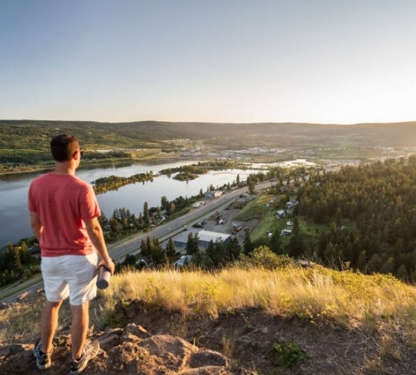 Mann steht auf einem Hügel und blickt auf den Williams Lake und die umliegende Landschaft. Kanada-Rundreise