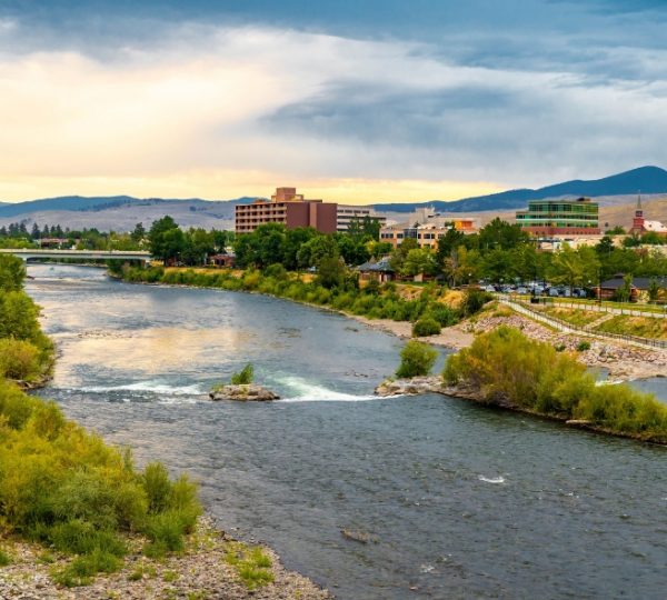 Flusslandschaft mit Bäumen und Gebäuden in Missoula unter einem bewölkten Himmel. Kanada-Rundreise