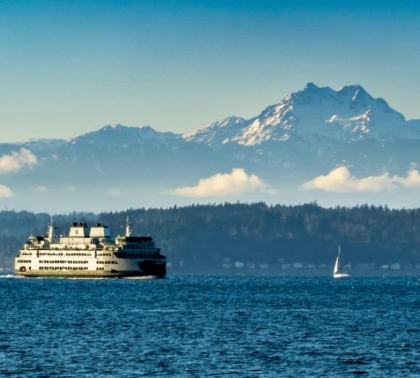 Eine Fähre fährt auf dem Wasser mit schneebedeckten Bergen im Hintergrund. Kanada-Rundreise