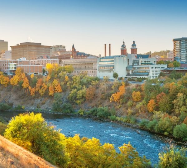 Blick auf die Stadt Spokane mit einem Fluss und herbstlichen Bäumen im Vordergrund. Kanada-Rundreise