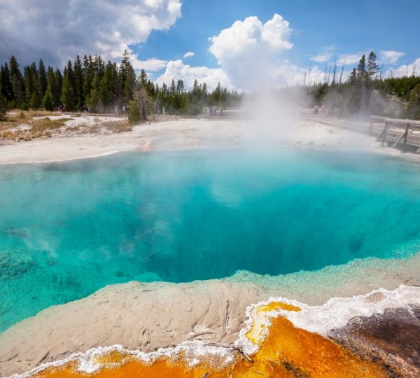 Eine geothermal Quelle im Yellowstone Nationalpark mit klarem, blauem Wasser und orangefarbenen Ablagerungen am Rand. Kanada-Rundreise