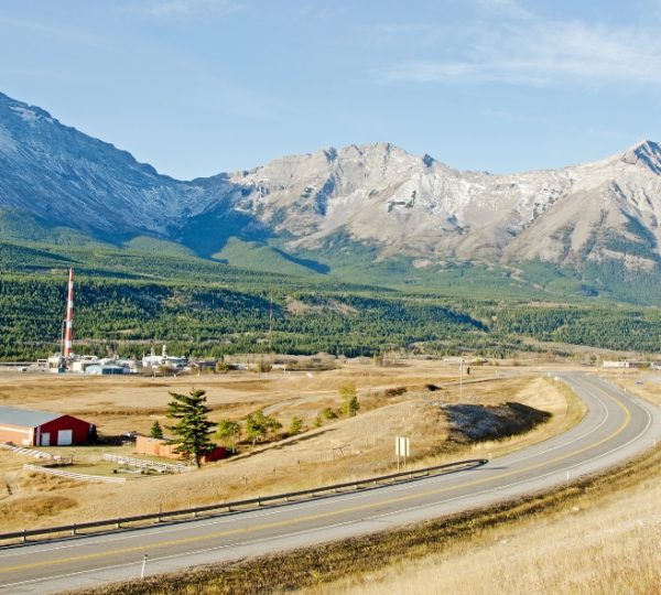 Landschaft mit Bergen im Hintergrund und einer Straße im Vordergrund, die durch eine offene Fläche führt. Kanada-Rundreise