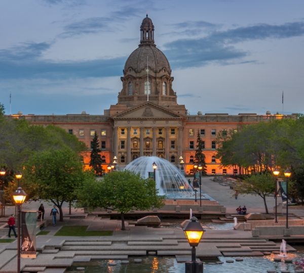 Das Regierungsgebäude von Edmonton mit einer Brunnenanlage und Bäumen im Vordergrund bei Dämmerung. Kanada-Rundreise