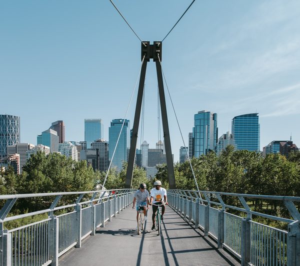 Zwei Personen gehen über eine Fußgängerbrücke in Calgary mit der Skyline im Hintergrund. Kanada-Rundreise