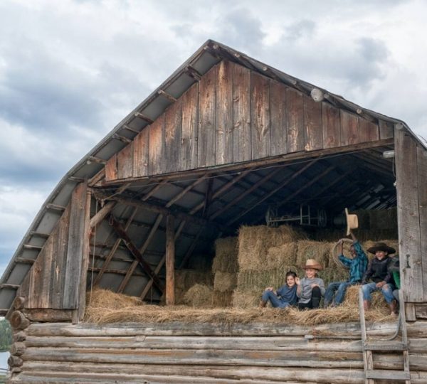 Personen sitzen in einer Scheune auf Heuballen mit Holzstruktur und Dach. Kanada-Rundreise