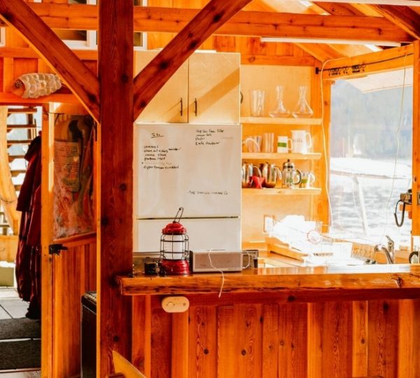 Inneneinrichtung einer Lodge mit Holzverkleidung, Küchenelementen und einem Fenster mit Blick auf Wasser. Kanada-Rundreise