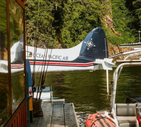 Wasserflugzeug von Ocean Pacific Air am Ufer eines Gewässers, umgeben von Bäumen. Kanada-Rundreise