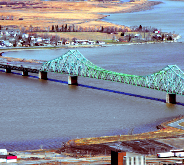 Grüne Brücke über einen Fluss in Campbellton mit umliegenden Wohngebäuden im Hintergrund. Kanada-Rundreise