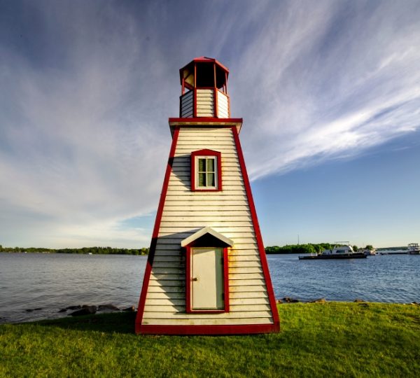 Ein Leuchtturm mit rotem Dach und weißen Wänden steht am Ufer eines Gewässers. Kanada-Rundreise
