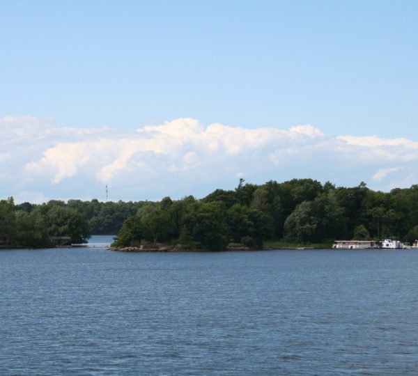 Ruhiges Gewässer mit mehreren kleinen Inseln und Booten im Hintergrund unter einem blauen Himmel. Kanada-Rundreise