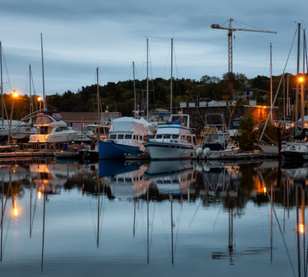 Boote im Hafen bei Dämmerung mit reflektierenden Wasserflächen und beleuchteten Masten. Kanada-Rundreise