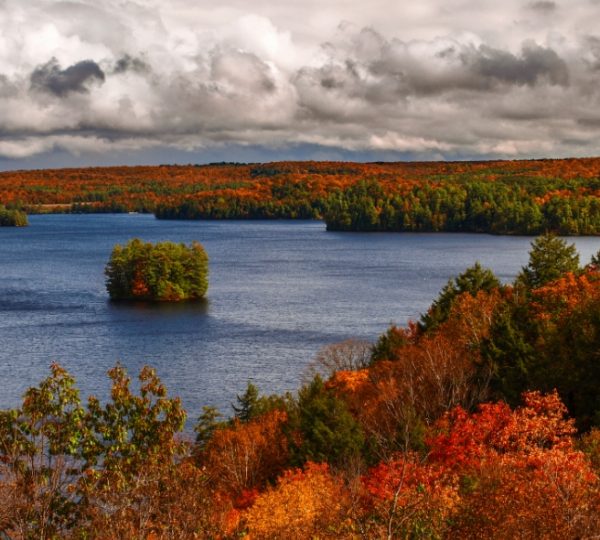 Blick auf einen See umgeben von herbstlichen Bäumen in verschiedenen Farben. Kanada-Rundreise