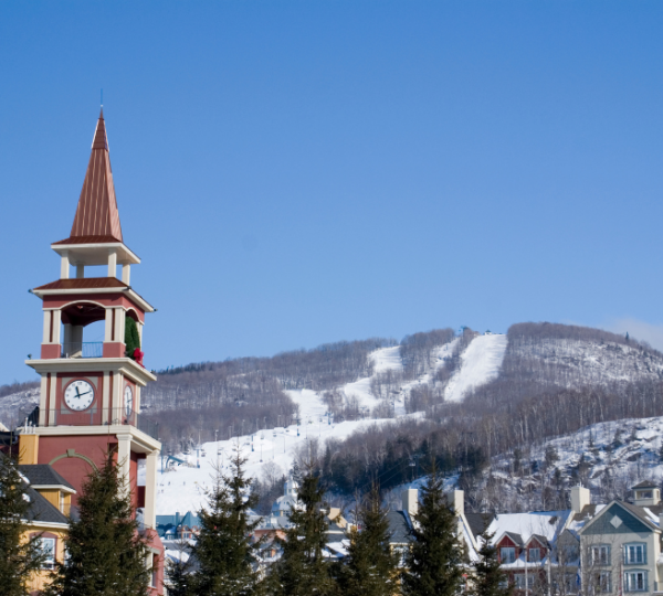 Uhrturm mit rotem Ziffernblatt und schneebedecktem Berg im Hintergrund in Mont Tremblant. Kanada-Rundreise