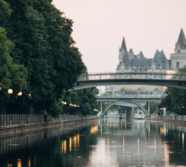 Auf Ostkanada Reise: Kanal in Ottawa mit einer Brücke und einem Schloss im Hintergrund, umgeben von Bäumen. Kanada-Rundreise