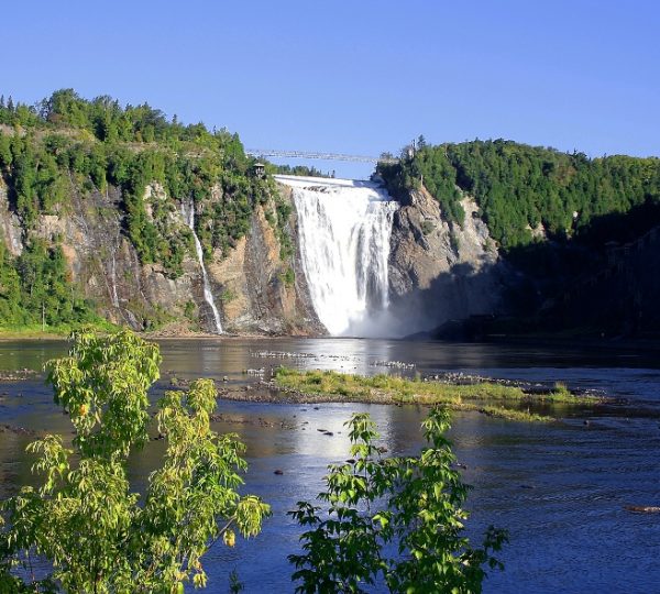 Wasserfall in Quebec mit umgebenden Bäumen und klarem Himmel. Kanada-Rundreise