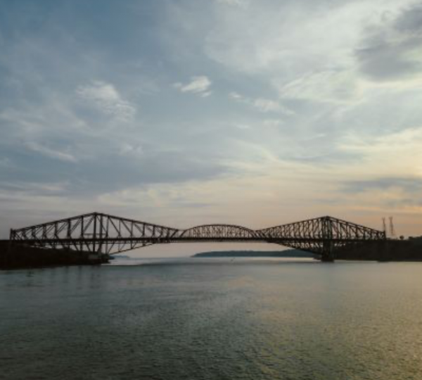 Eisenbahnbrücke über einen Fluss bei Sonnenuntergang mit Wolken am Himmel. Kanada-Rundreise