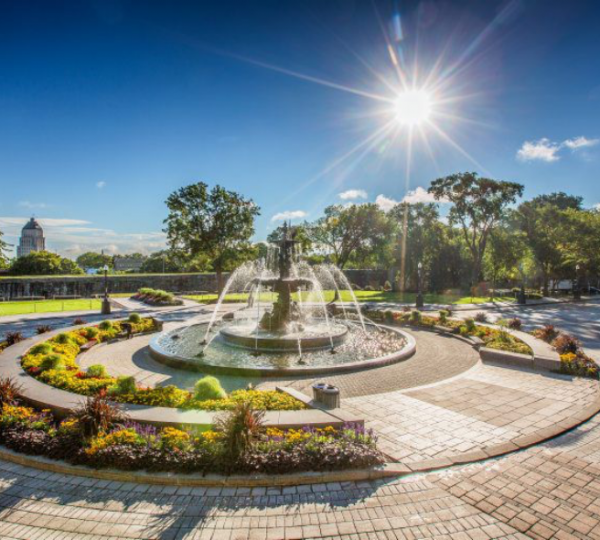 Brunnen mit Wasserstrahlen in einem Stadtpark, umgeben von Blumenbeeten und Bäumen. Kanada-Rundreise