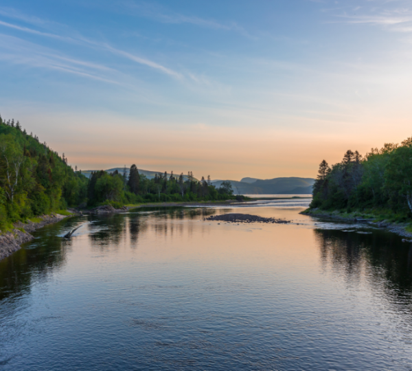 Ruhevolle Flusslandschaft mit Bäumen und sanften Hügeln im Hintergrund bei Sonnenuntergang. Kanada-Rundreise