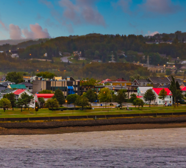 Bunte Häuser in Saguenay mit roten Dächern und grünen Bäumen entlang der Uferlinie. Kanada-Rundreise