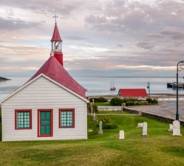 Kapelle mit rotem Dach und grünen Türen in Tadoussac, Kanada, mit Blick auf das Wasser und die Boote. Kanada-Rundreise
