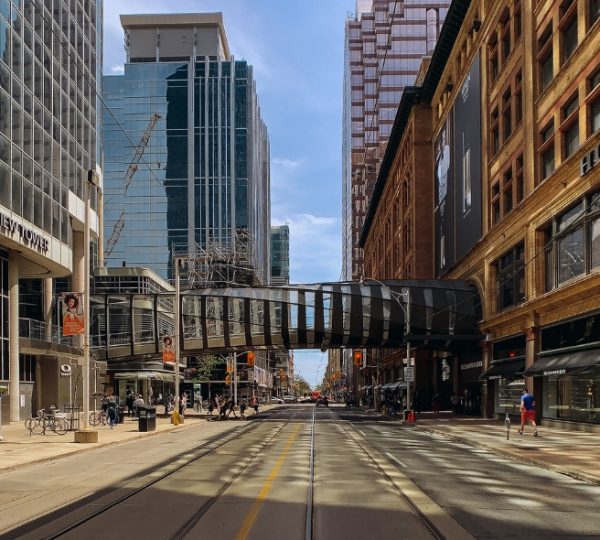 Blick auf eine Stadtstraße in Toronto mit modernen Hochhäusern und einer Fußgängerbrücke. Kanada-Rundreise