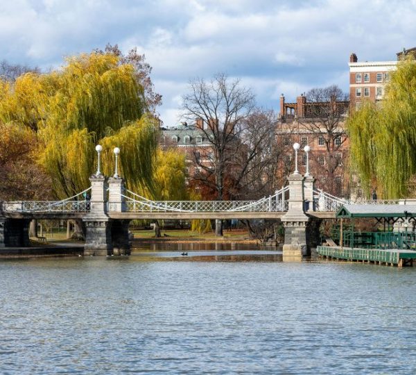 Eine Brücke mit Laternen über einem See, umgeben von Bäumen und Gebäuden in Boston. Kanada-Rundreise