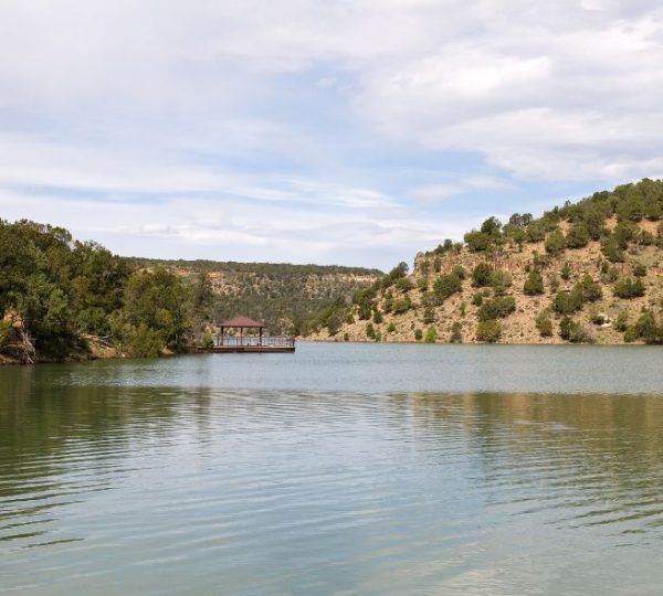 Ruhiger See mit einem Holzsteg und bewaldeten Hügeln im Hintergrund unter einem bewölkten Himmel. Kanada-Rundreise