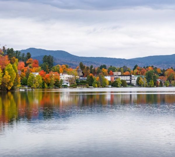 Herbstliche Farben am Lake Placid mit reflektierendem Wasser und bewaldeten Ufern. Kanada-Rundreise