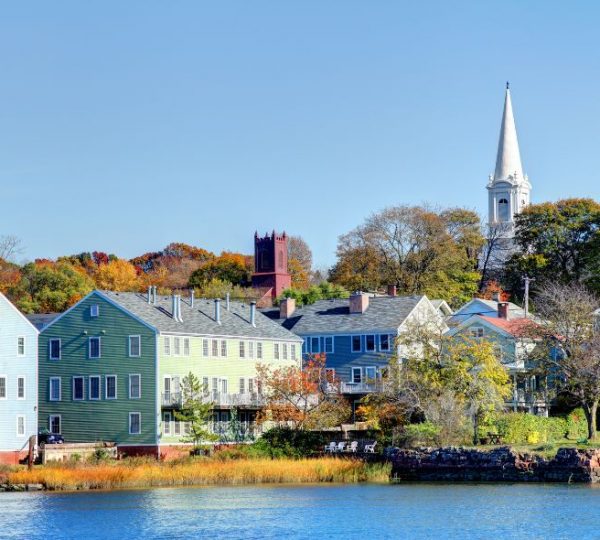 Bunte Häuser am Wasser in New Haven, Ostkanada, mit einem Kirchturm im Hintergrund. Kanada-Rundreise