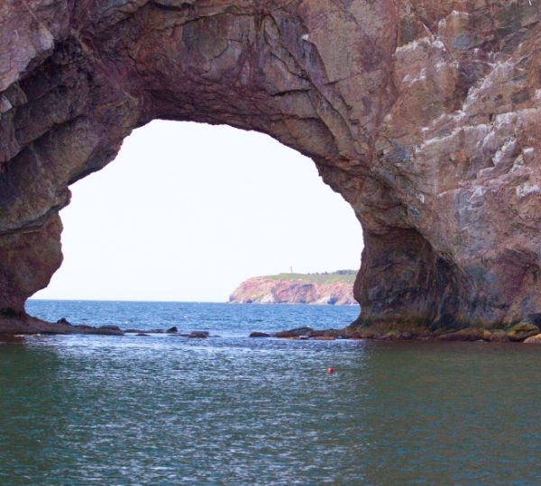 Natürlicher Felsbogen mit Blick auf das Meer und die Küste im Hintergrund. Kanada-Rundreise