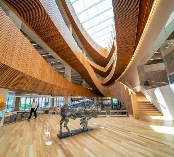 Innenraum eines modernen Gebäudes mit einer Holzstruktur und einer Bison-Skulptur aus Metall. Kanada-Rundreise