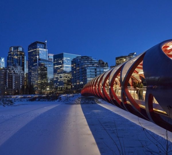 Der Peace Bridge in Calgary, eine rote Fußgängerbrücke, beleuchtet bei Nacht mit modernen Gebäuden im Hintergrund. Kanada-Rundreise