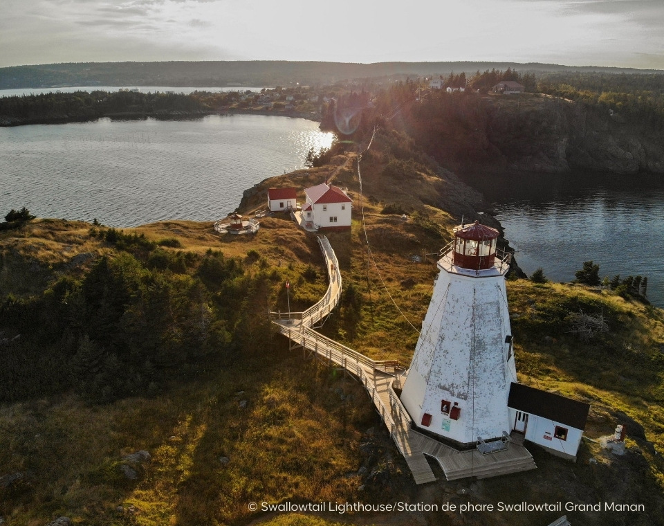 Leuchtturm von Swallowtail auf Grand Manan, umgeben von Wasser und Natur, mit einem Holzsteg, der zum Gebäude führt. Kanada-Rundreise