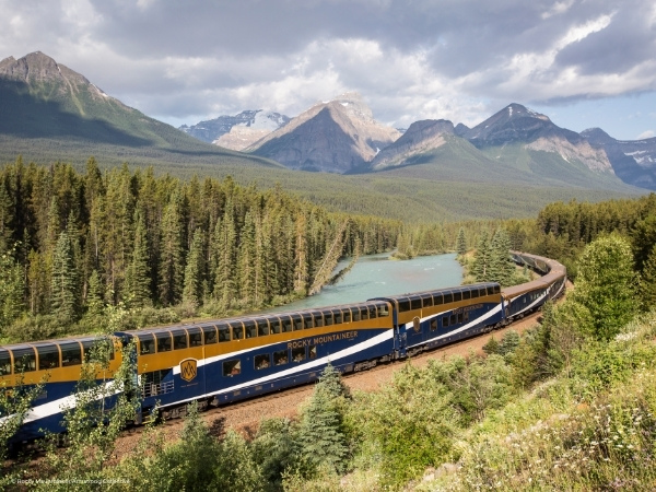 Rocky Mountaineer Zug, der durch die kanadischen Rocky Mountains fährt, umgeben von Bergen und Wald. Kanada Zugreise