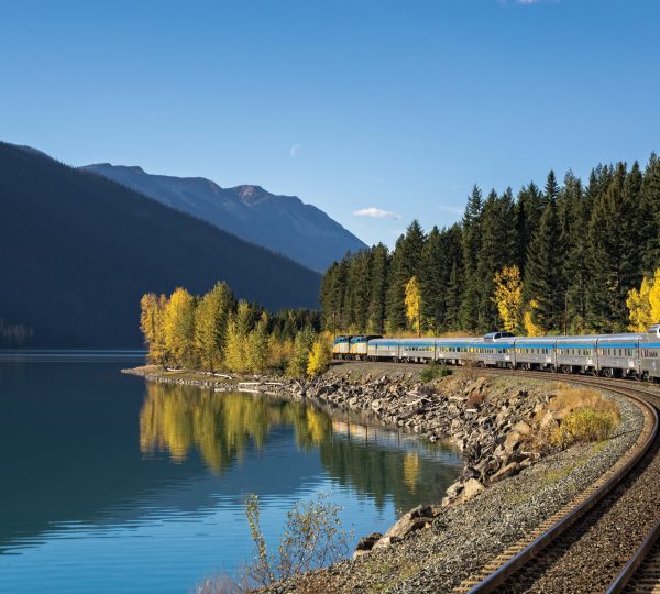 Ein VIA-Zug fährt entlang des Moose Lake, umgeben von Bergen und Bäumen in Kanada. Kanada-Rundreise
