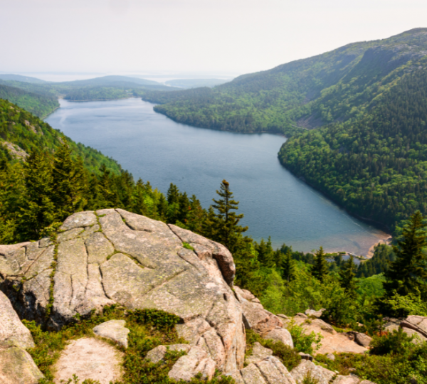 Acadia National Park Blick über felsigen Felsvorsprung, umliegende grüne Wälder, ruhiger See und Berglandschaft rund um Bar Harbor Kanada-Rundreise