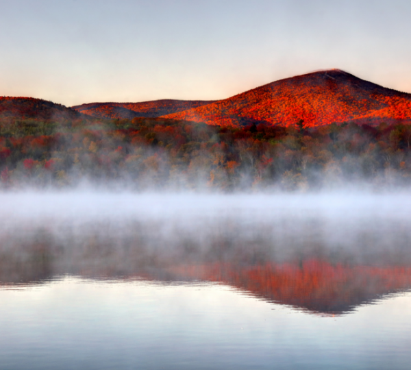 Killington Vermont: Herbstliche Berglandschaft mit roten Herbstblättern, nebelverhangener See und sanften Bergen im Hintergrund Kanada-Rundreise