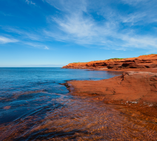 Rote Felsen-Küste von Prince Edward Island vor klarem Meer und blauem Himmel; markante rote Gesteinsschichten, ruhiges Wasser, maritime Landschaft Kanada-Rundreise