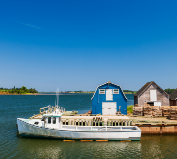 Blick über ruhigen Hafen mit weißem Boot vor einem blauen Fischerhaus und weiteren Holzhäusern; Prince Edward Island, Nova Scotia inspiriert, maritime Küstenstimmung Kanada-Rundreise