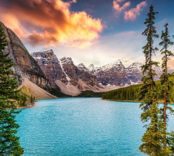 Moraine Lake in Banff mit intensiv blaugrünem Wasser, umliegenden Tannen, felsigen Bergen und dramatischem Sonnenuntergang am Himmel Kanada-Rundreise