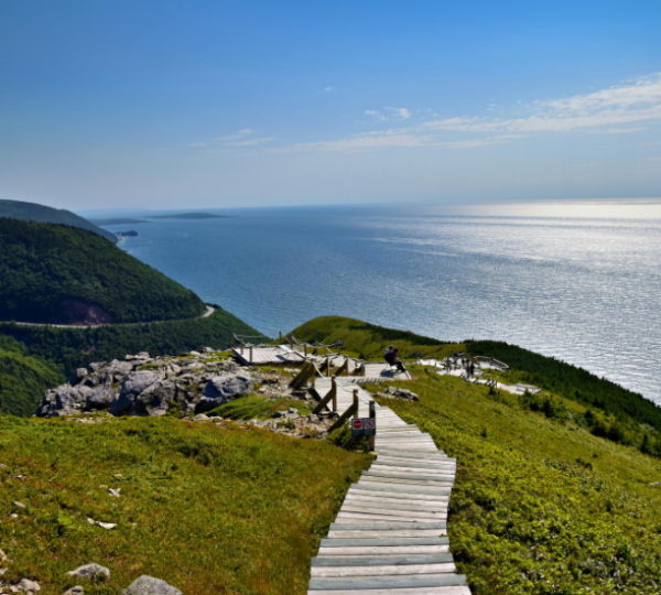 Cape Breton Highlands National Park auf Cape Breton Island: grüne Hügellandschaft, Holzstegpfad, ruhiges Meerpanorama, blauer Himmel und sonnige Küste Kanada-Rundreise