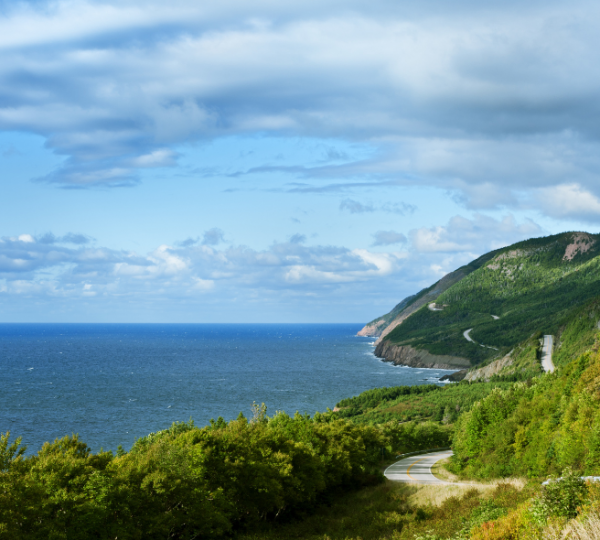 Blick über die blaue See entlang einer kurvenreichen Küstenstraße durch grüne Hügel im Cape Breton Island Gebiet, Baddeck-Region, Halifax Umgebung Kanada-Rundreise