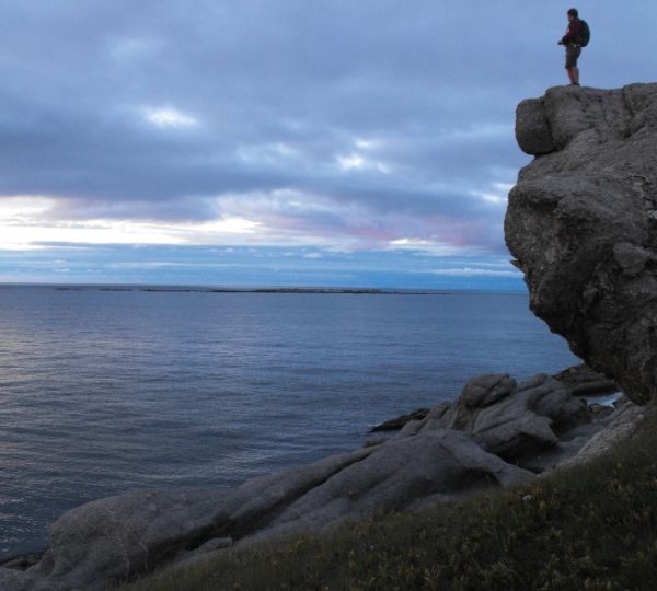 Wanderer steht auf einer felsigen Klippe über dem ruhigen Meer vor Halifax und Cape Breton, raues Küstenpanorama, farbiger Himmel, CharloTTown-Atmosphäre Kanada-Rundreise