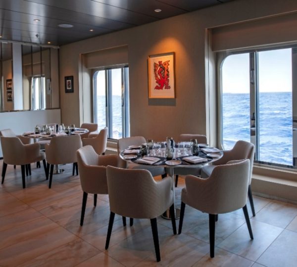 Eleganter Speisesaal auf der Scenic Eclipse mit hellen Stühlen, gedeckten Tischen und Blick aufs offene Meer während einer Arktis-Kreuzfahrt Kanada-Rundreise