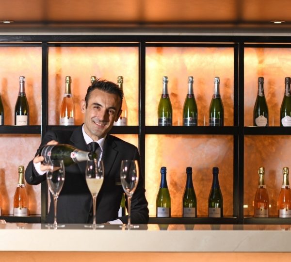 Luxuriöse Bar an Bord der Scenic Eclipse: Barpersonal schenkt Champagner ein, eingerahmt von glänzenden Flaschen und stilvollen Gläsern. Kanada-Rundreise