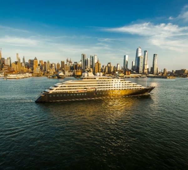 Scenic Eclipse Kreuzfahrtschiff gleitet vor der Skyline von New York City durch ruhiges Wasser, majestätische Hochhäuser im Hintergrund, Abendlicht reflektiert auf der Wasseroberfläche, Luxuskabinen an Bord Kanada-Rundreise