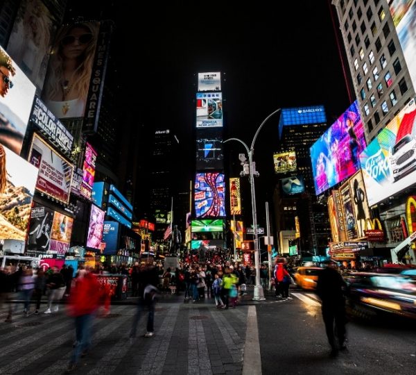 Bunte Werbetafeln und Menschenmengen in Times Square, New York City, bei Nacht; leuchtende Anzeigen, vorbeifahrende Taxis und lebendiges urbanes Treiben. Kanada-Rundreise